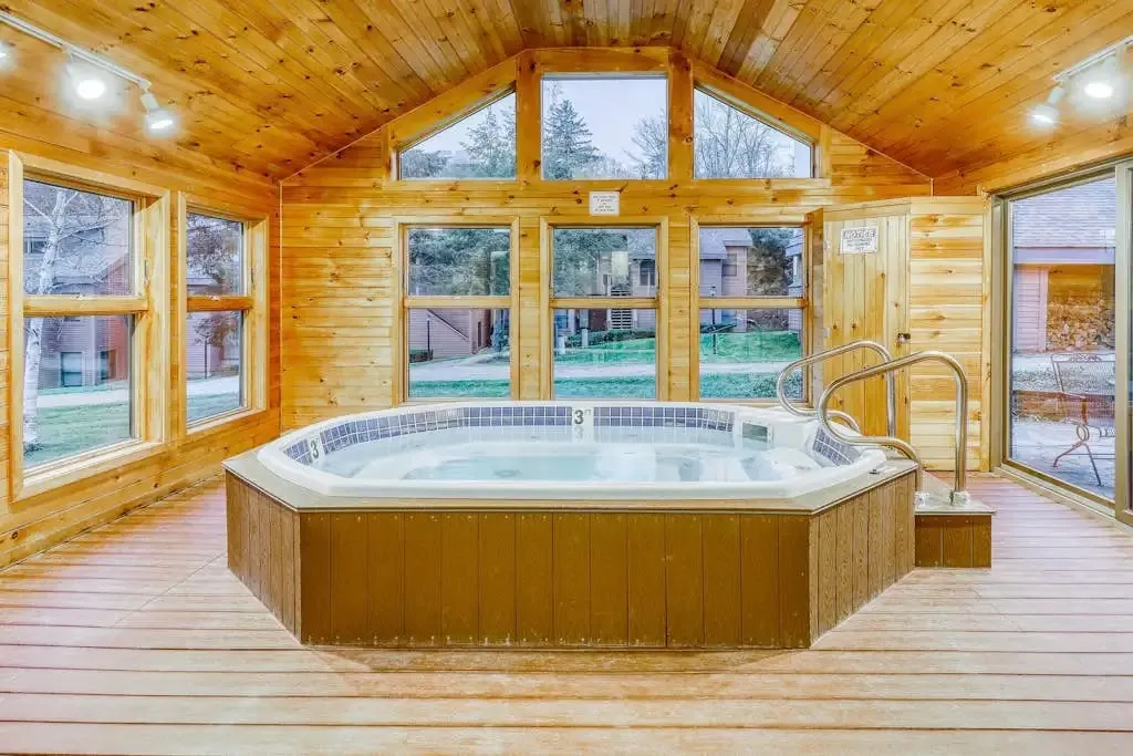 Octagonal hot tub in a wood-paneled sunroom with large windows overlooking the grounds