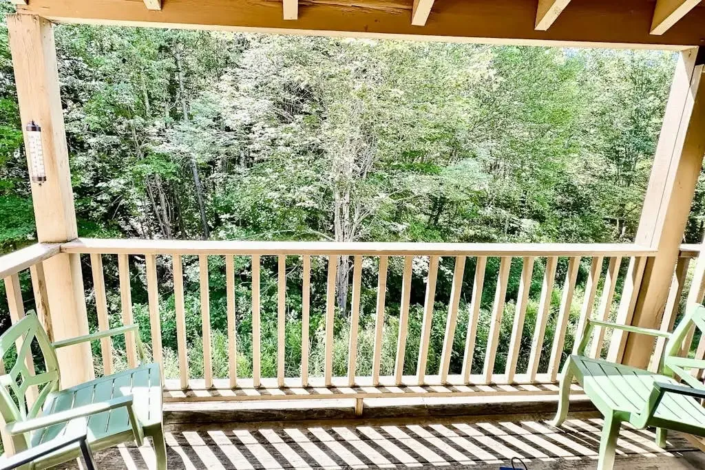 Covered balcony with wooden railing and seating surrounded by dense green trees