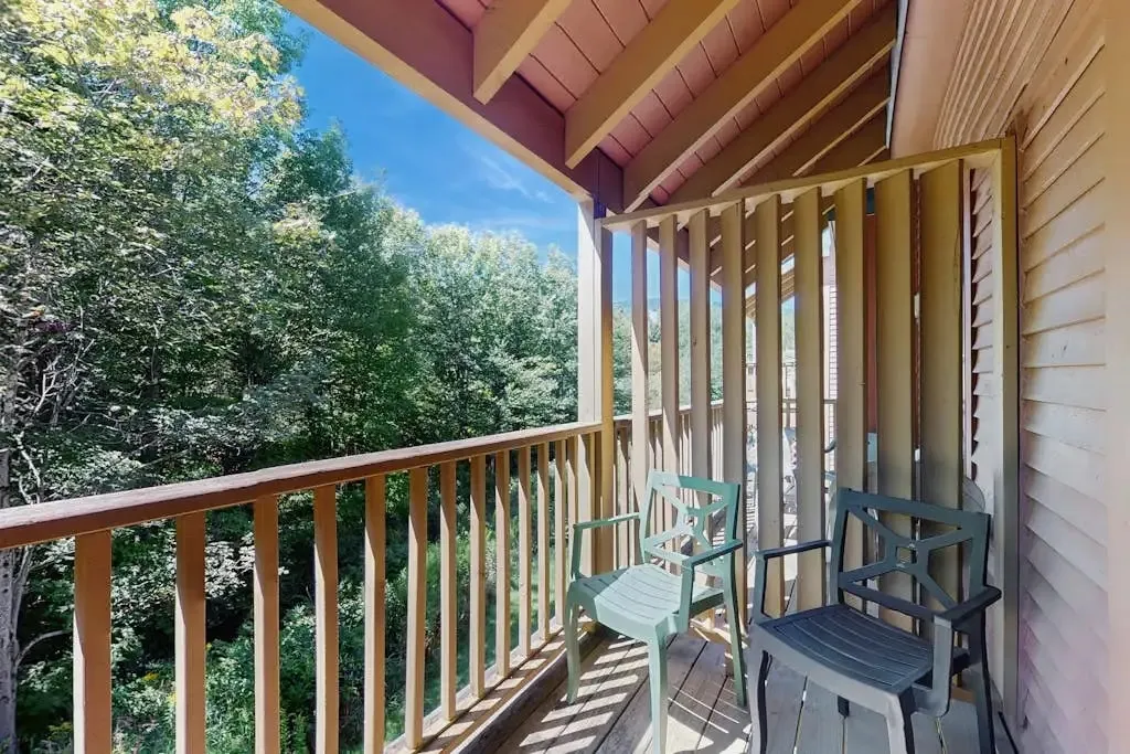 Balcony with patio chairs overlooking a wooded hillside under a blue sky