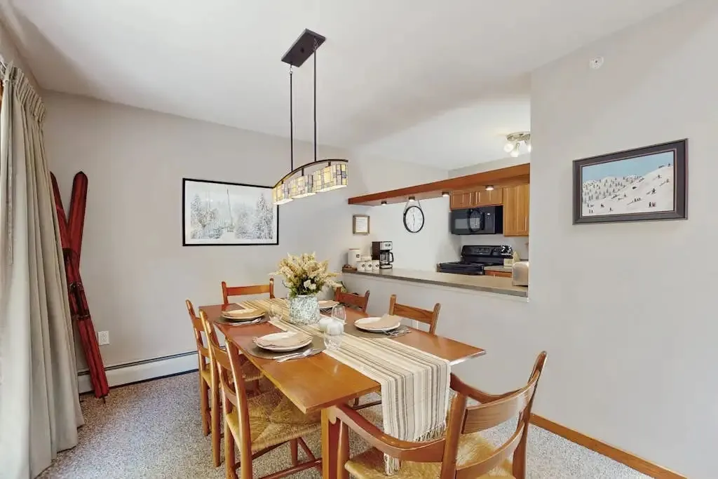 Dining table set for six with a pendant light, next to a pass-through opening to the kitchen