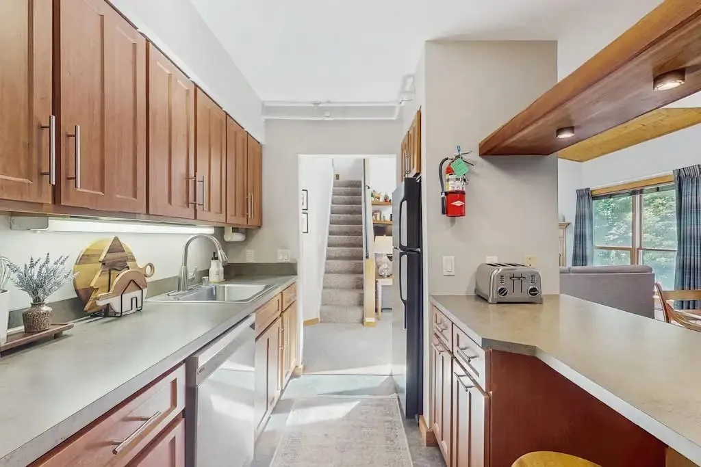 Kitchen with wood cabinetry, stainless steel sink and dishwasher, and a view toward the stairs