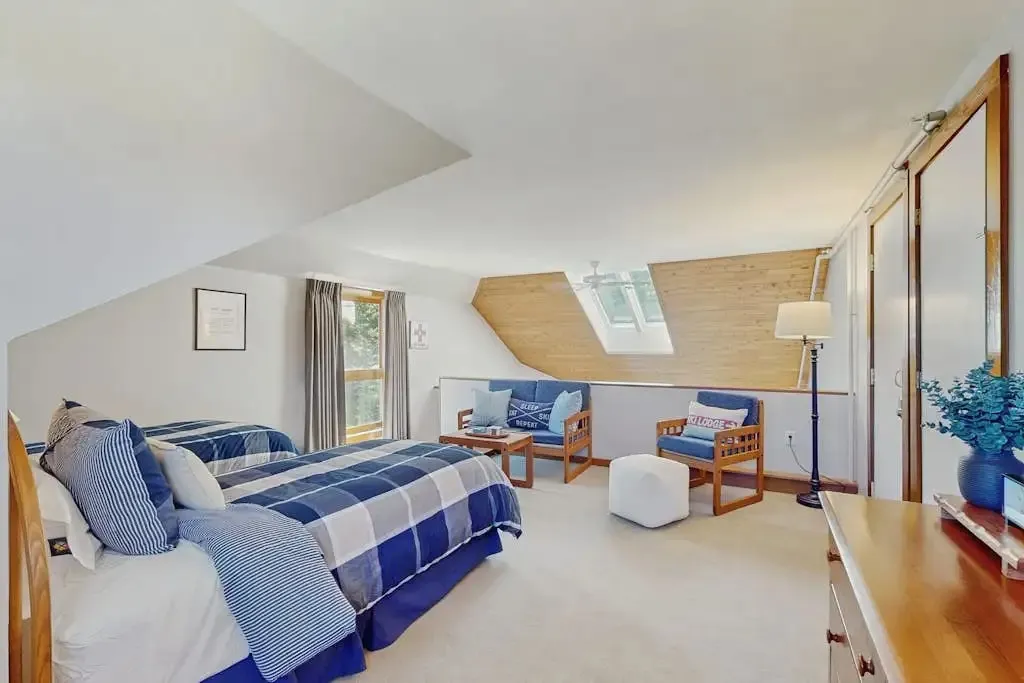 Loft with two twin beds in blue plaid bedding, a skylight dormer, and a small lounge seating area